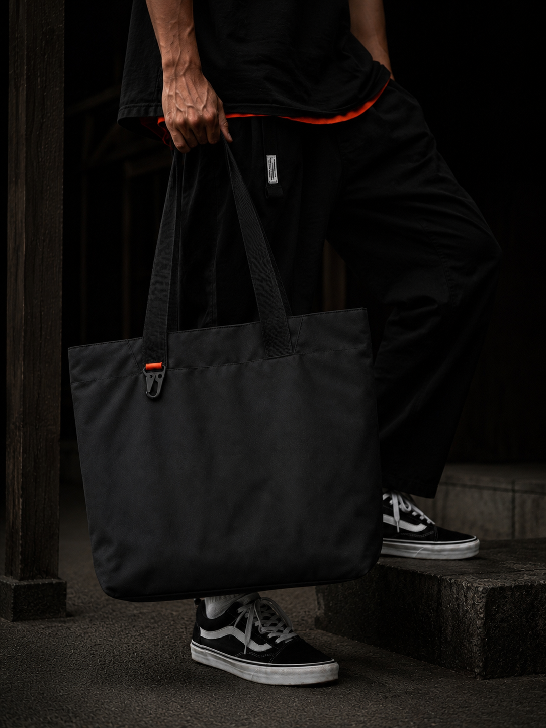 MAY.BE Utility Prime black tote, Drop 001, hanging against concrete wall